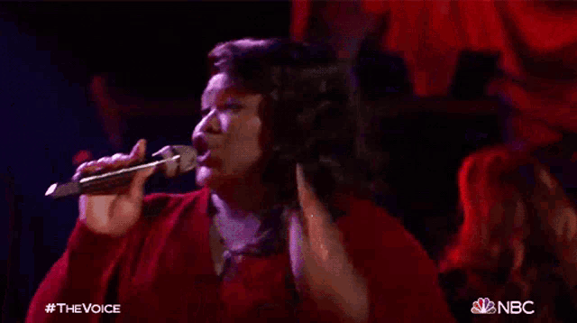 a woman singing into a microphone with the nbc logo on the bottom