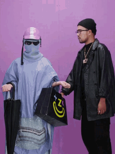 a man in a black jacket is holding a black bag with a yellow smiley face on it
