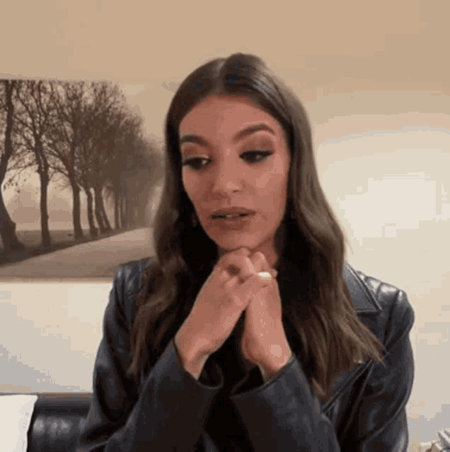 a woman in a black leather jacket is sitting in front of a picture of trees