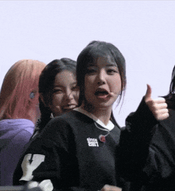 a girl wearing a black sweater with the letter y on the sleeve gives a thumbs up