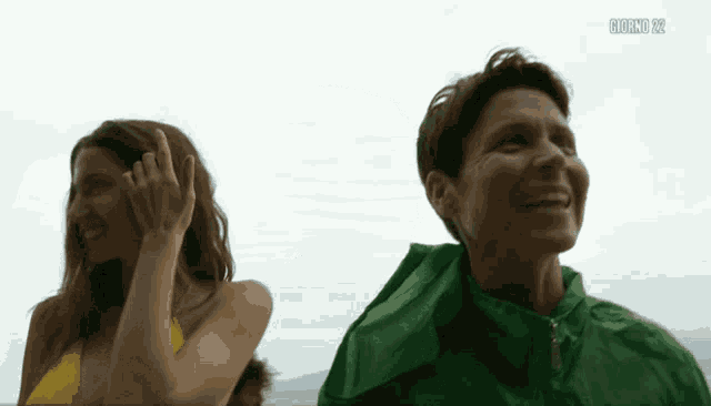 a woman in a green jacket stands next to another woman in a yellow bikini