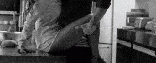 a black and white photo of a man and a woman having sex on a kitchen counter .