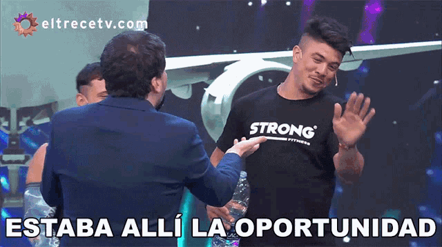 a man wearing a strong t-shirt talks to a man in a suit