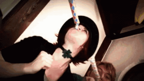 a woman wearing a hat and a green clover necklace is blowing a party horn .