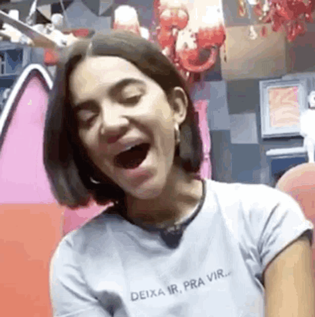 a woman is laughing with her mouth open and wearing a white shirt .