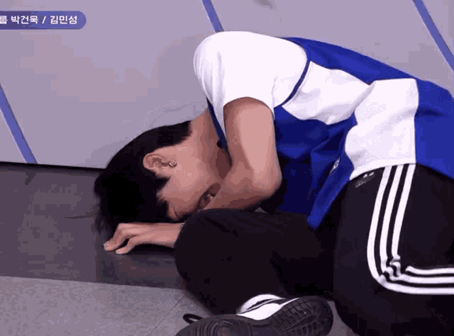 a man in a blue and white shirt laying on the floor with his head down