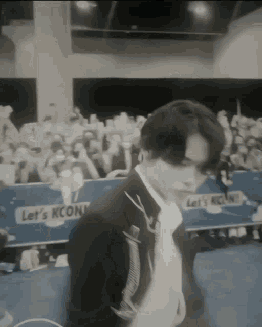 a man in a suit stands in front of a crowd with a sign that says let 's kcon