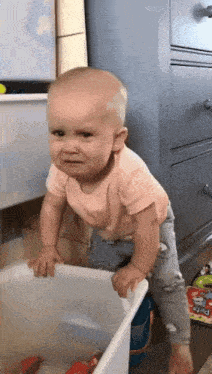 a baby is crying while standing next to a white bin .