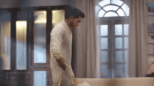 a man in a white shirt is walking towards a couch in a living room .