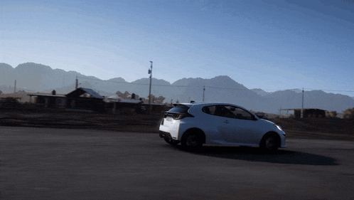 a white car is driving down a road with a mountain in the background