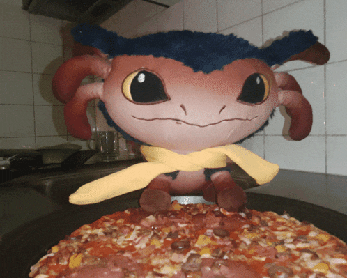 a stuffed animal wearing a yellow scarf sits on a pizza