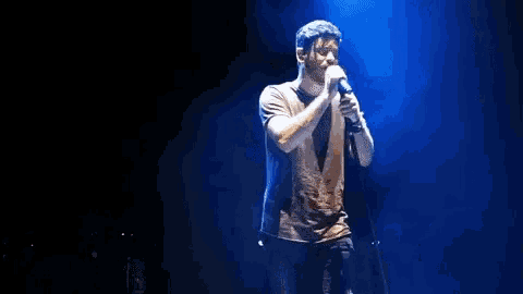 a man is singing into a microphone on a stage with blue lights behind him