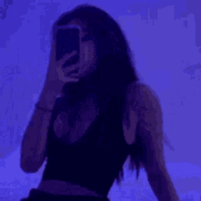 a woman is taking a selfie with her cell phone in front of a purple wall .