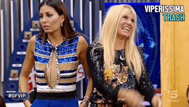 two women are standing next to each other on a stage and one of them is wearing a blue and gold top .