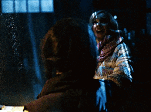 a woman with a scarf around her neck is talking to another woman in the dark