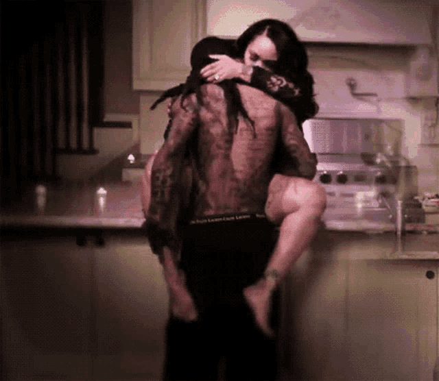 a man is carrying a woman in his arms in a kitchen wearing a pair of black underwear that says calvin klein love