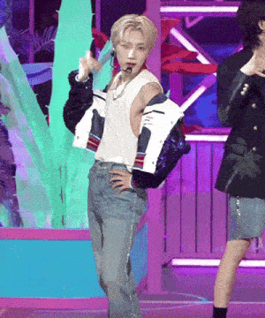a man wearing a white tank top and a jacket is standing on a stage with his hands on his hips