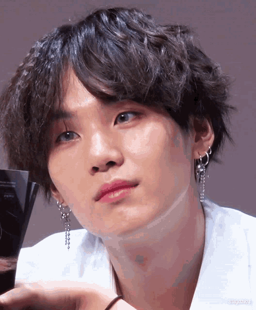 a close up of a young man 's face with a white shirt and earrings