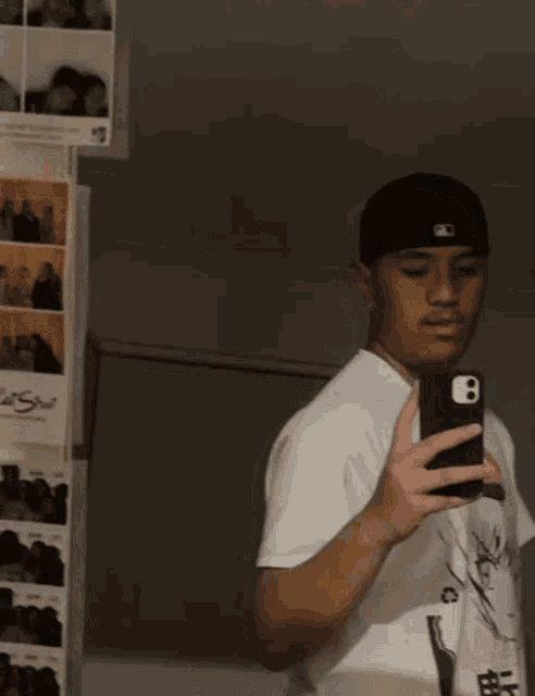 a young man is taking a picture of himself in a mirror while wearing a black hat with the number 8 on it