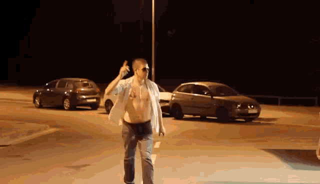 a shirtless man with a tattoo on his chest walks down a parking lot at night