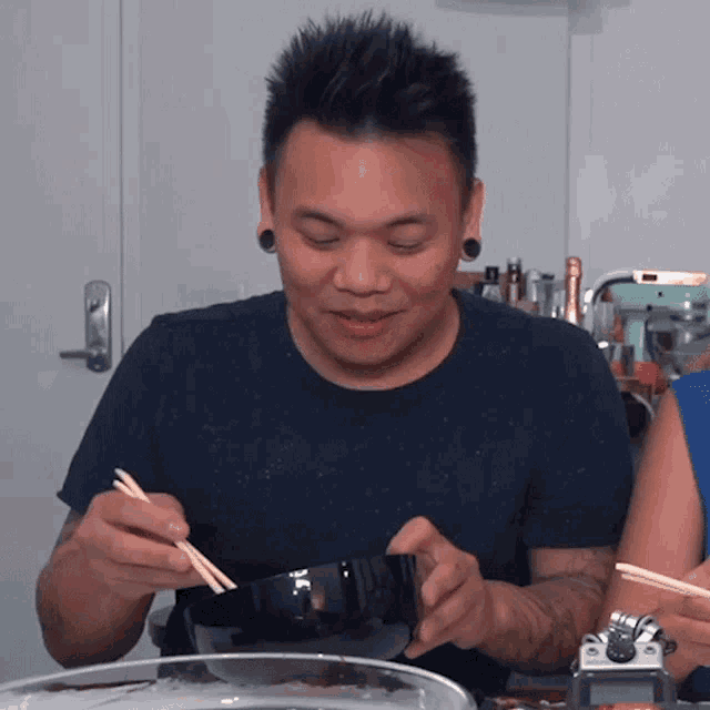 a man in a blue shirt is holding chopsticks in his right hand