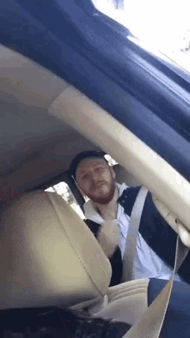 a man with a beard is sitting in the back seat of a car wearing a seat belt