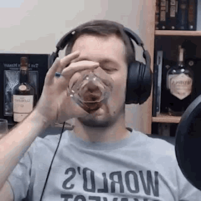 a man wearing headphones and a t-shirt is drinking a glass of whiskey .