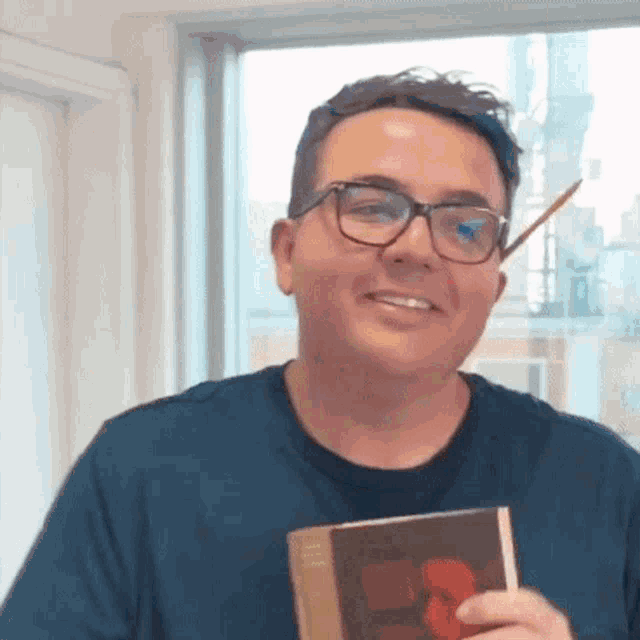 a man wearing glasses is smiling while holding a book and a pencil in his mouth