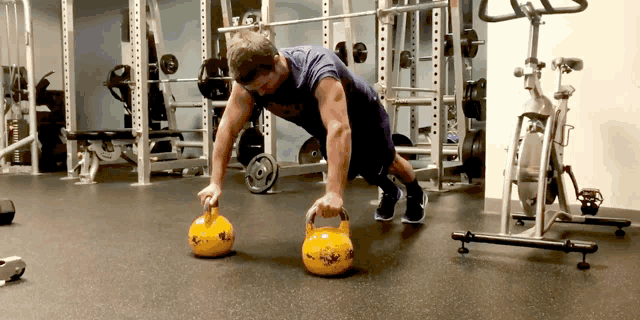 a man in a purple shirt is doing push ups with a yellow kettlebell