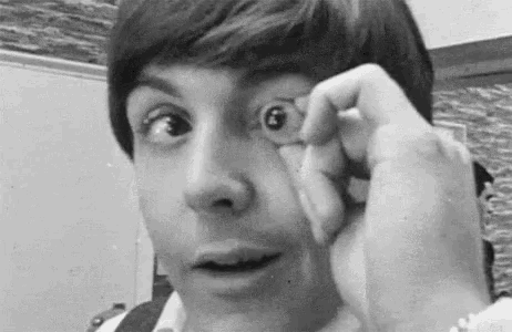 a black and white photo of a man holding a small object to his eye .