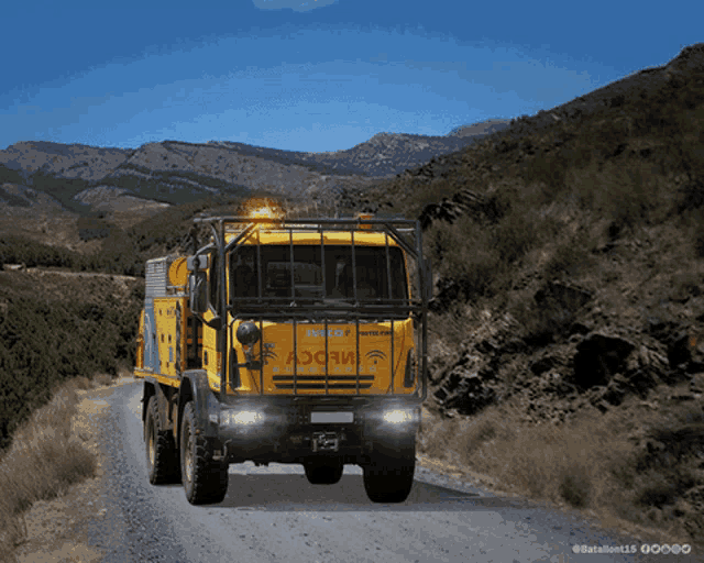 a yellow truck with the word iveco on the front drives down a dirt road