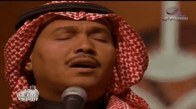 a man singing into a microphone with arabic writing on the bottom right