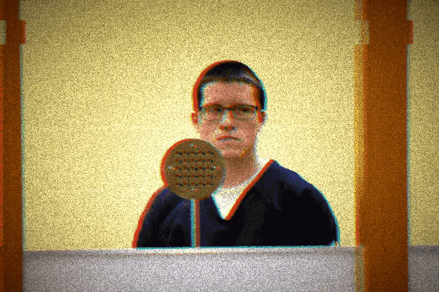 a man with glasses stands in front of a microphone with a yellow background