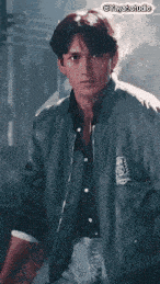 a man wearing a bomber jacket and a black shirt is standing in a dark room .