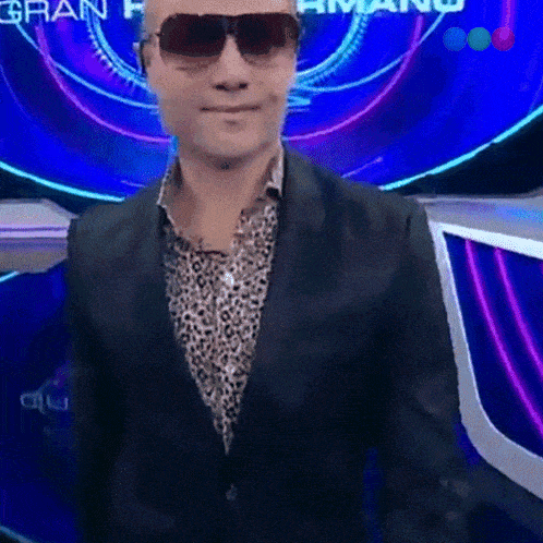 a man wearing sunglasses and a suit stands in front of a sign that says gran