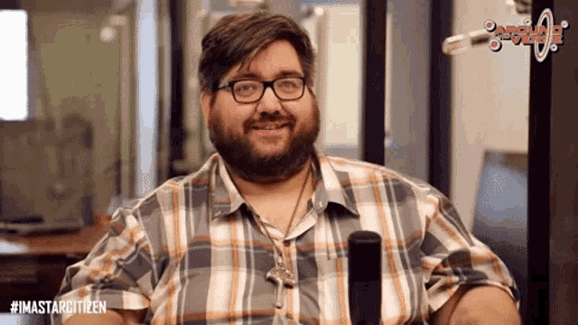 a man wearing glasses and a plaid shirt is sitting in front of a microphone with the hashtag #imastarcitizen