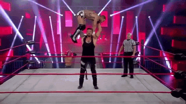 a wrestler is holding another wrestler up in the air in a wrestling ring .