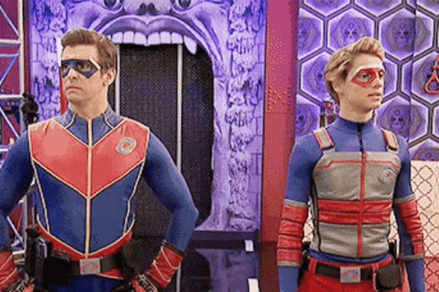 two men in superhero costumes are standing next to each other in front of a skull wall .