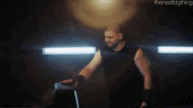 a man in a black tank top is standing in a dark room with a hammer in his hand .