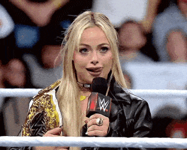a woman in a wrestling ring speaking into a microphone with a w logo on it
