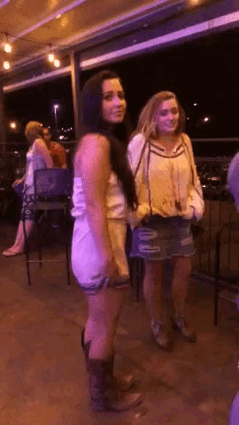two women standing next to each other on a balcony at night
