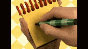 a person is writing on a yellow notepad with a green pen