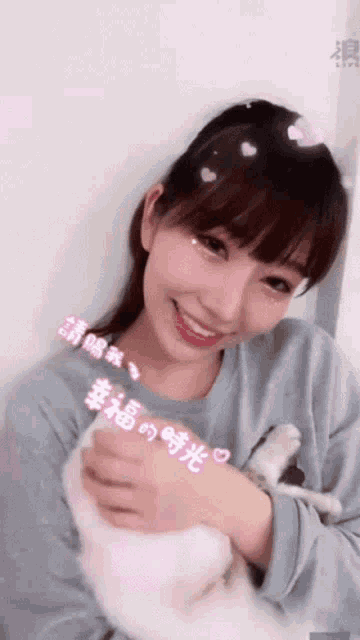a woman in a blue shirt is holding a white cat and smiling