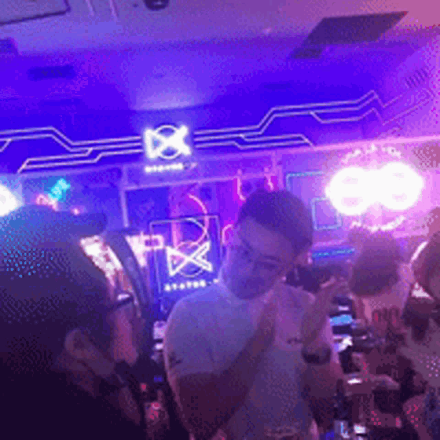 a group of people are gathered in a room with purple lights and a sign that says x on it