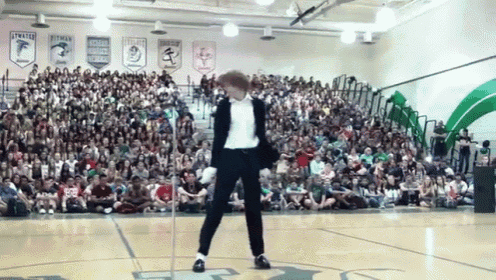 a man in a suit is dancing in front of a crowd in a gym with a banner that says stewart