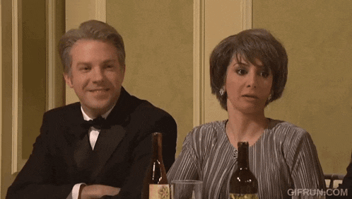 a man and a woman sit at a table with a bottle of wine and a glass