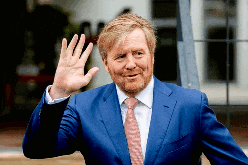 a man in a blue suit and red tie waves his hand