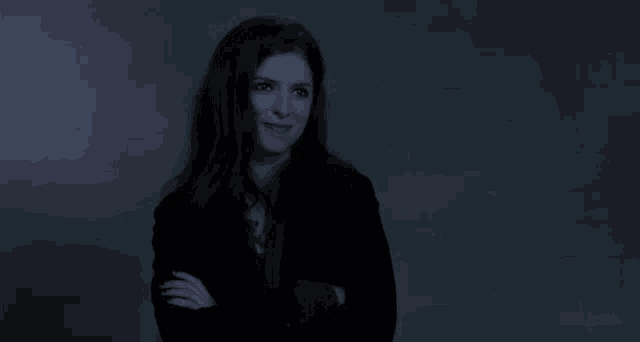 a woman in a black jacket is smiling with her arms crossed in front of a green wall .