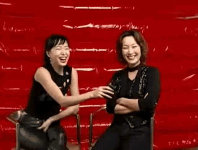 two women are sitting next to each other in front of a red background .