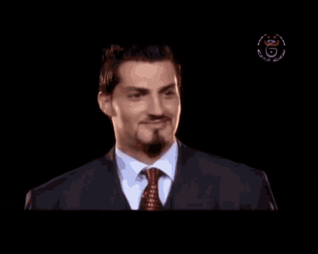a man in a suit and tie is smiling in front of a black background with a logo for algeria on it